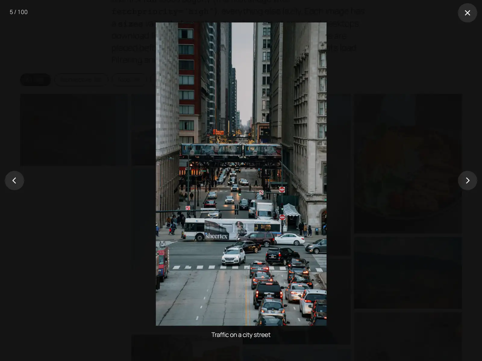 A dark full-screen lightbox showing a photo of a city street with an elevated train, with a counter 5 of 100, a close button and previous and next arrows